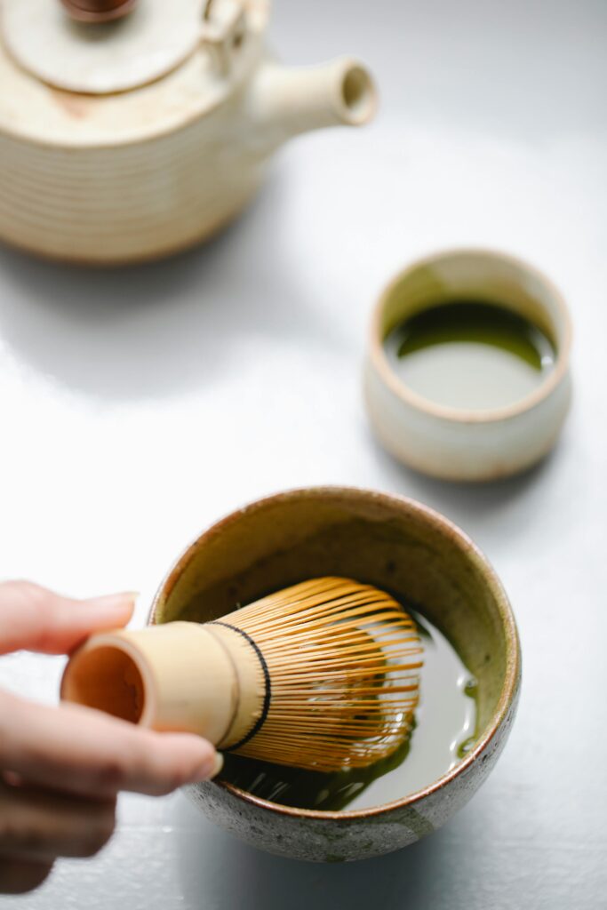 pexels-photo-5947093-5947093 Close-up of hands preparing matcha tea with whisk and cup, indoors.